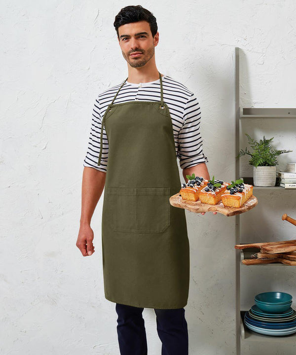 Man wearing a striped shirt and green apron holds a tray of assorted Premier PR181 sliced pastries with fruit toppings. Shelving with dishes and plants in the background.