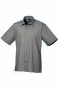 The Premier PR202 is a gray short-sleeve button-up shirt, featuring a front pocket and showcased on a white background. This shirt is designed with a pointed collar for a neat, casual appearance.