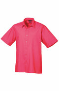 A short-sleeved button-up shirt with vibrant pink coloring, featuring a collar and a pocket on the left side, from the Premier brand's PR202 collection, displayed on a plain white background.