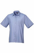 A short-sleeved button-up shirt from the Premier brand, model PR202, in light blue featuring a collar and a chest pocket, is displayed against a plain white background.