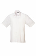 The Premier PR202 is a simple white, short-sleeved button-down shirt featuring a pocket on the left side. It comes with a classic collar and is showcased against a white background.