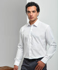 A man with dark, curly hair is wearing a white dress shirt and gray pants, standing in a modern, minimalistic interior with Premier's PR207.