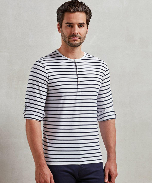 A man with short dark hair and a beard is wearing a white long-sleeve Premier PR218 shirt with black horizontal stripes and black pants, standing against a plain light-colored background.