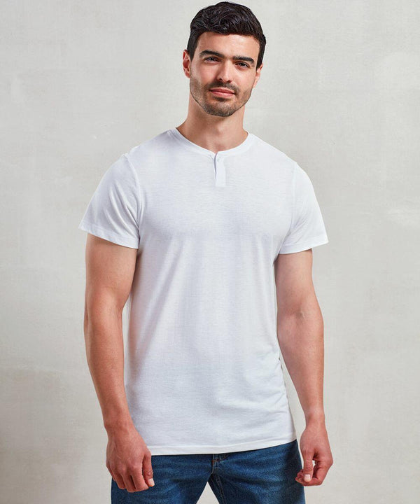 A man with dark hair and a beard is standing against a plain background, wearing a Premier PR219 white T-shirt and blue jeans.