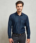 A man with short brown hair and a beard is standing and looking at the camera, wearing a dark denim shirt and dark grey PR222 pants by Premier.