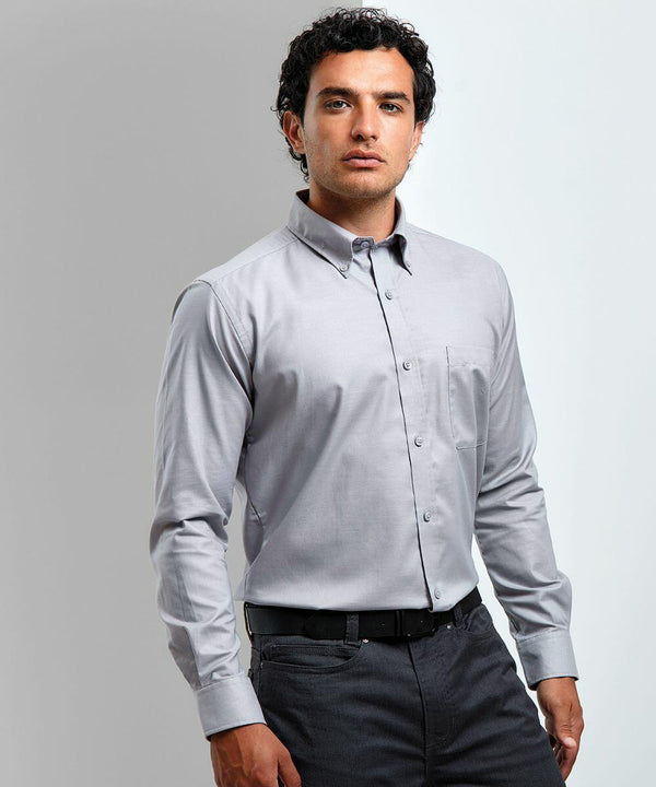 A man with short curly hair is wearing a light grey PR234 button-up shirt by Premier and dark grey pants, standing against a light background.