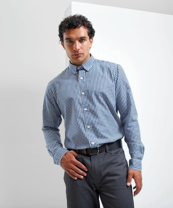 A man stands against a plain white background, wearing a Premier PR252 long-sleeved blue and white checkered shirt tucked into gray pants.