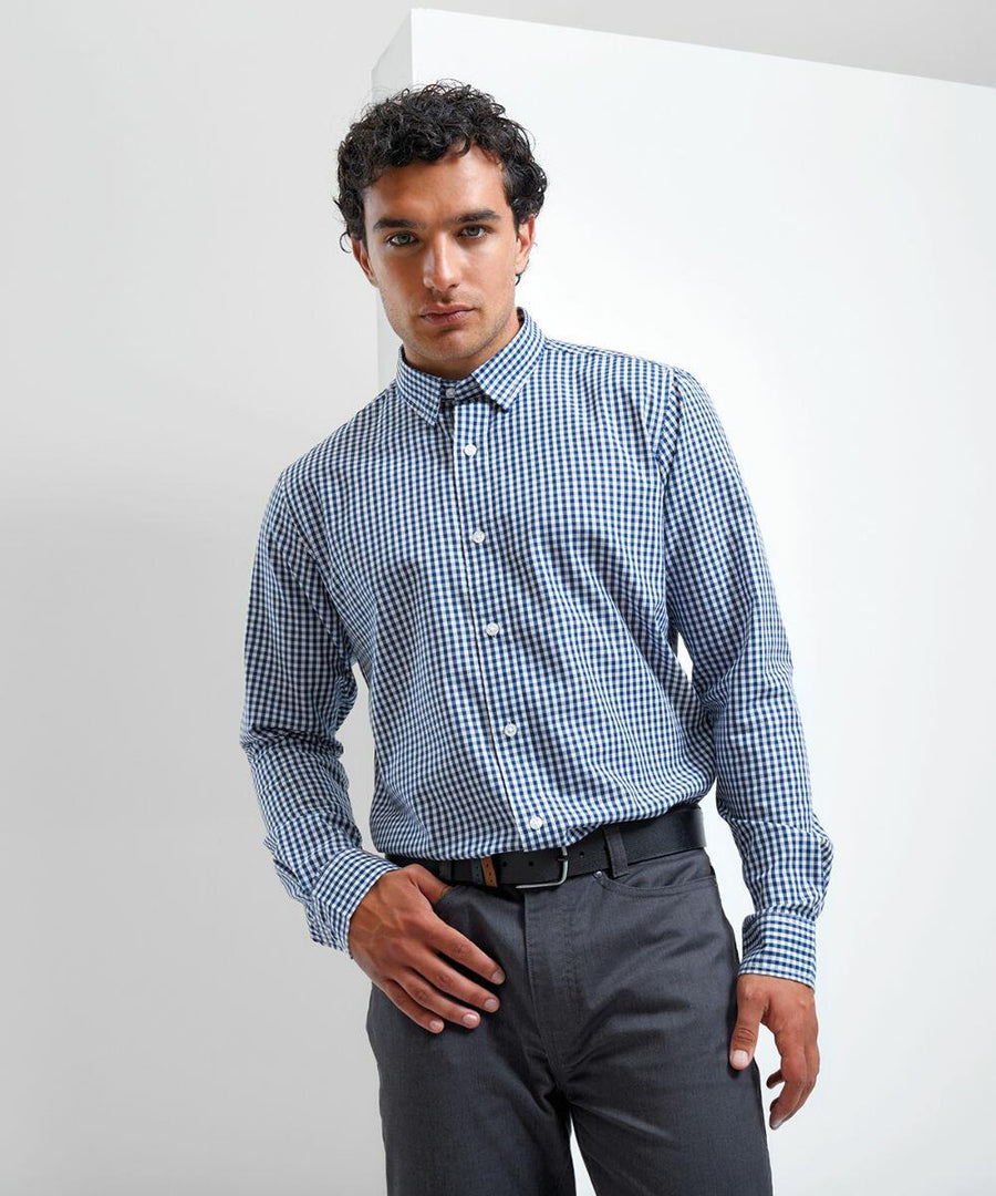 A man stands against a plain white background, wearing a Premier PR252 long-sleeved blue and white checkered shirt tucked into gray pants.