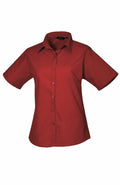 The Premier PR302 is a classic design featuring a short-sleeved, red button-down shirt with a pointed collar. It is displayed flat against a white background to emphasize its simplicity and timeless style.