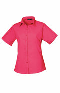 The Premier PR302 is a vibrant pink short-sleeve button-up shirt featuring a classic collar, showcased against a plain white background.