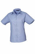 A Premier PR302 light blue button-up shirt, featuring short sleeves and a classic collar, displayed on a white background.