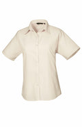 Introducing the PR302 by Premier, a beige button-up shirt featuring short sleeves and a classic collar, elegantly showcased against a plain white background.
