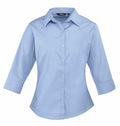 Premier's PR305 women's shirt features a light blue color, button-up design, three-quarter sleeves, and a collar, all showcased against a white background.