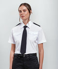A person with a neutral expression is wearing a white short-sleeved shirt with two breast pockets, a black tie, black epaulets, and black pants from Premier's PR312 line.