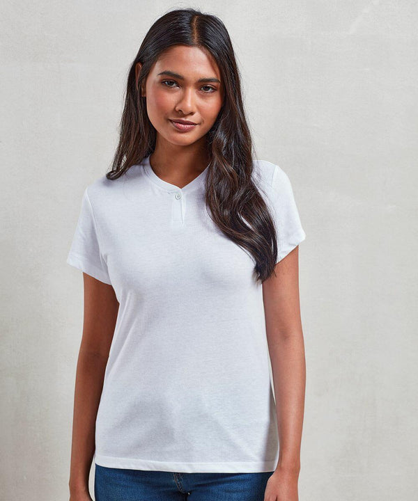 A woman with long dark hair is wearing a white short-sleeved Premier PR319 and jeans, standing against a plain off-white background.