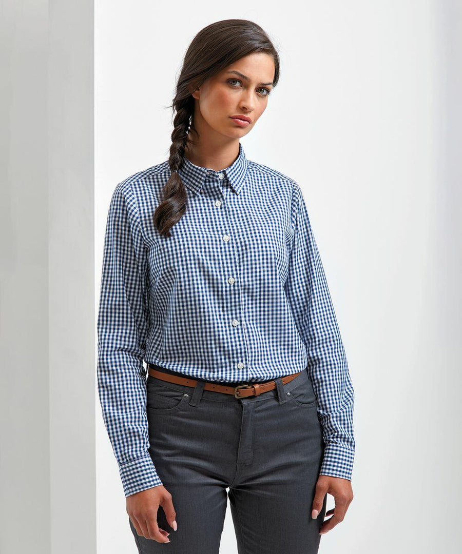 A woman with long braided hair is wearing a Premier PR352 blue checkered shirt and dark gray pants, standing against a plain white background.