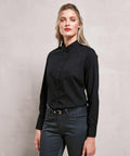 A person with blonde hair is standing against a plain background, wearing a long-sleeve black button-up shirt, PR358 by Premier, and grey pants.