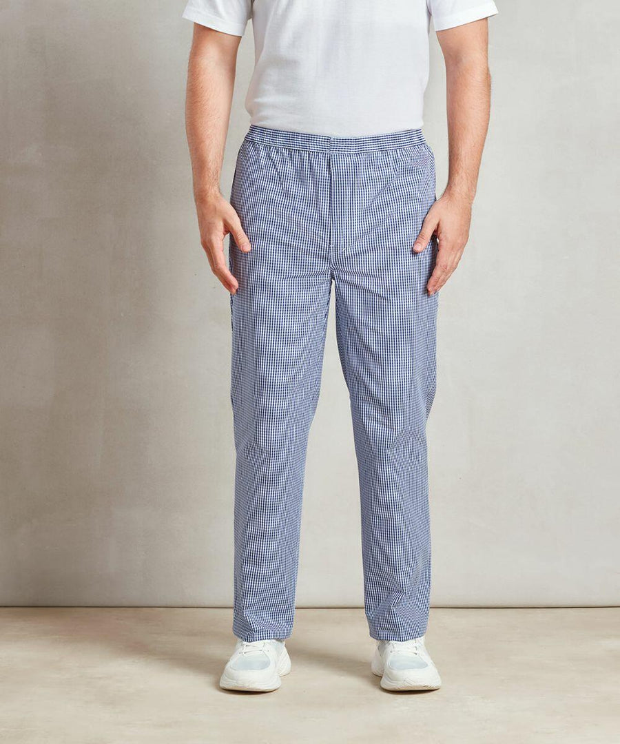 A person stands with their arms at their sides wearing a white Premier PR552, blue and white checkered pants, and white shoes.