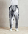 Person wearing Premier PR553 black and white checkered pants, a white top, and white shoes, standing against a neutral background.