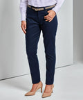 A person dressed in a light-colored shirt, dark blue trousers, and beige Premier PR570 high-heeled shoes stands with one hand resting on their hip.