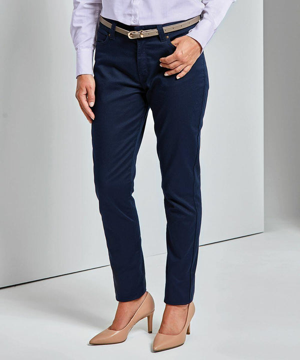 A person dressed in a light-colored shirt, dark blue trousers, and beige Premier PR570 high-heeled shoes stands with one hand resting on their hip.