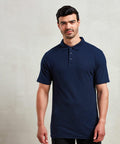 A person standing against a plain background, wearing a Premier PR610 navy blue polo shirt.
