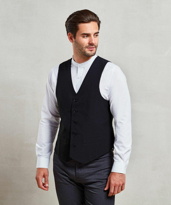 A man with short dark hair, wearing a white shirt, a black buttoned vest, and gray trousers, stands against a plain light-colored wall featuring the Premier PR622.