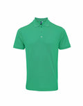 The Premier PR630 is a plain green polo shirt with short sleeves and a classic collar. It includes a three-button placket and is displayed against a white background.