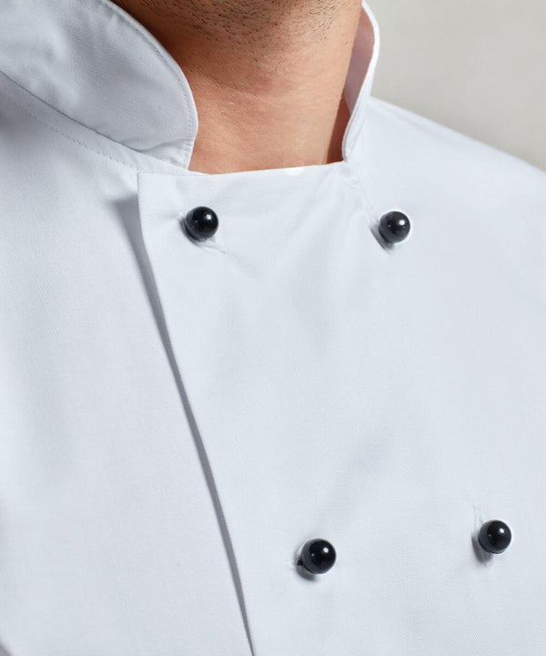 Close-up of a person wearing a white double-breasted Premier PR652 chef's jacket with black buttons. The top button is open, revealing part of their neck.