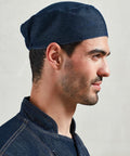 A man in profile wearing a Premier PR653 dark blue denim cap and matching jacket, standing against a plain light gray background.