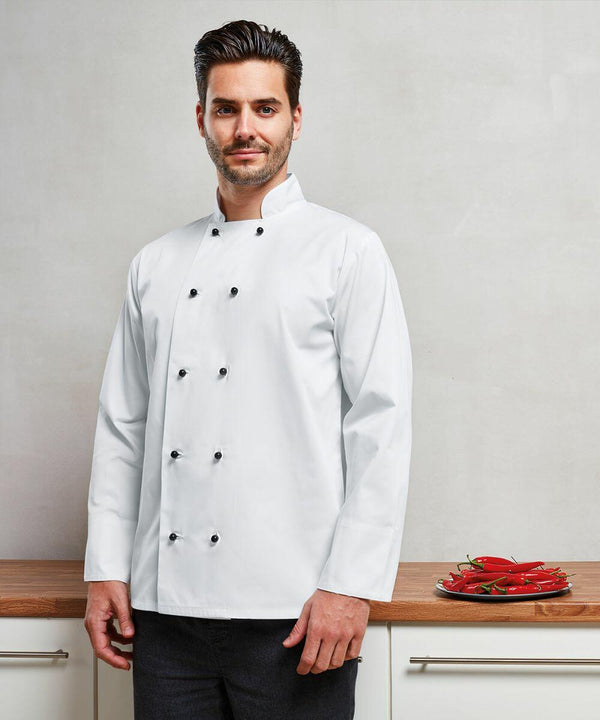 A man in a white chef's jacket stands in a kitchen next to a wooden counter with a plate of Premier PR661 red chili peppers.