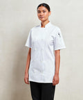 A person stands against a plain background wearing a double-breasted, short-sleeved white Premier PR670 chef's jacket and black pants.