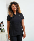 Person wearing a black short-sleeved uniform stands in a room with white walls, next to a table holding Premier PR683 beauty products.