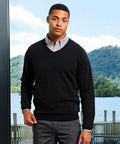 A person standing indoors wearing a black V-neck sweater over a gray shirt with a scenic view of trees and water visible through a window behind them is sporting the Premier PR694.