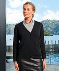 A woman in a black PR697 cardigan by Premier and grey shirt stands by a window, with a scenic outdoor background featuring a lake and trees.