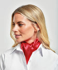 A person with blonde hair wearing a white Premier PR730 shirt and a red scarf tied around their neck, looking slightly to the side.