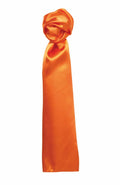 A sophisticated PR730 satin scarf by Premier features a glossy orange finish and is artistically knotted at one end. The silky smooth fabric exhibits a subtle shine, catching the light beautifully. Positioned against a white background, the scarf's vibrant color and rich texture are prominently displayed.