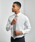 A man in a white Premier PR785 dress shirt adjusts his gray tie while looking to the side.