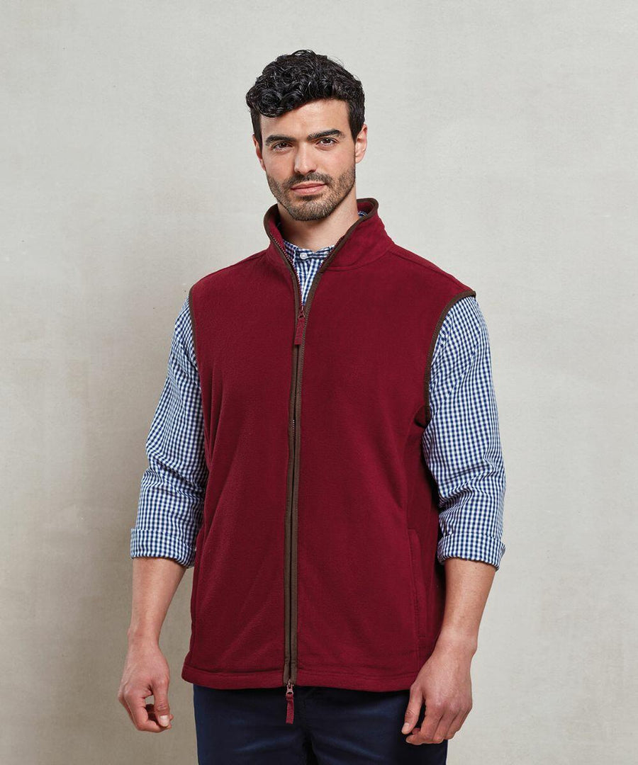 A man with dark hair and a beard wears a Premier PR803 red zip-up fleece vest over a checkered shirt, standing against a plain background.
