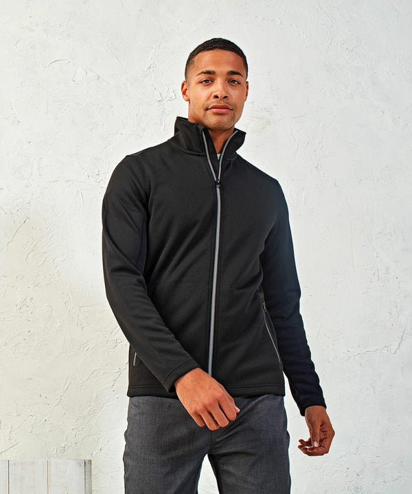 A person in a black zip-up Premier PR808 jacket poses against a light-colored, textured wall, with one hand slightly raised.