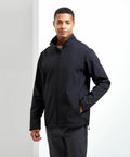 A person wearing a black Premier PR810 jacket stands with their hand in the pocket and slightly smiles at the camera.