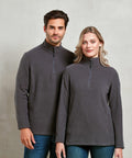 Two individuals stand side by side, wearing matching gray Premier PR831 quarter-zip fleece tops and blue jeans, posing against a plain background.