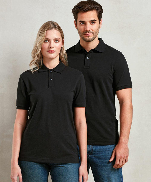 A woman and a man, both wearing black PR995 Premier polo shirts and blue jeans, stand side by side against a plain light-colored background.
