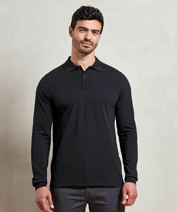 A man with short dark hair is wearing a black long-sleeved Premier PR997 polo shirt and grey pants, standing against a plain light-colored background.