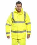 A man wearing a bright yellow Portwest PW003 with reflective stripes stands facing forward with a serious expression.
