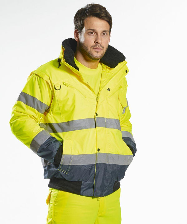 A man wearing a bright yellow high-visibility jacket with reflective stripes, branded as the Portwest PW013, stands against a plain white background. Hands are in pockets, and he appears to be looking off to the side.