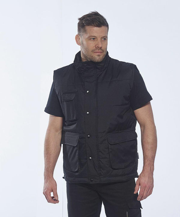 A man stands against a plain background, wearing a black short-sleeve shirt and a black Portwest PW027 utility vest with multiple pockets.