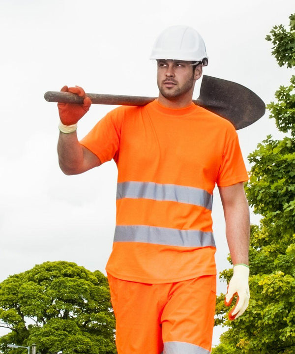 A man wearing a white hard hat, orange high-visibility shirt and pants, and gloves, holds a Portwest PW090 over his shoulder while standing outdoors.