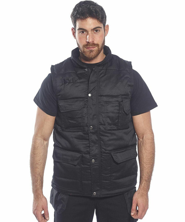 Man wearing a black **Portwest PW169** vest over a black t-shirt. The vest has multiple pockets and snap buttons. He stands against a plain white background.