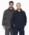 Two people standing side by side wearing Portwest PW171 zip-up fleece jackets. The person on the left is wearing a gray jacket, and the person on the right is wearing a navy blue jacket. They are looking at the camera.